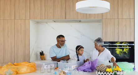 Biracial grandparents and granddaughter sort recyclables in a modern kitchen
