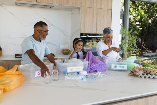 Biracial grandparents and granddaughter sort recycling in a bright kitchen