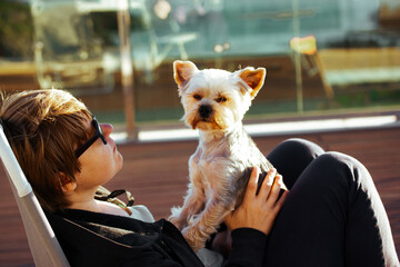 Happy woman with her little Yorkshire terrier dog on the hands relaxing outdoors on a sunny...