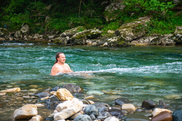 Tranquil Mountain River Setting with a Man with Long Hair Swimming Amidst Trees and Rocky Landscape