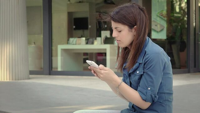 young woman messaging with her smartphone sitting in the city