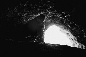 a black and white photo of a person looking out of a cave