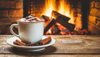 Fotobehang hot chocolate in a mug on wooden table with cozy fireplace flame on the background © Yesenia