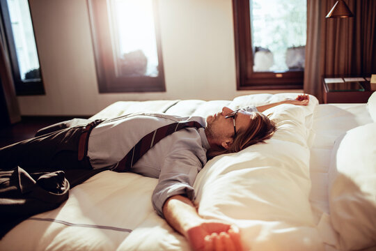 Mature businessman lying down in a bed in a hotel room