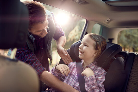 Father putting seatbelt on daughter in car backseat