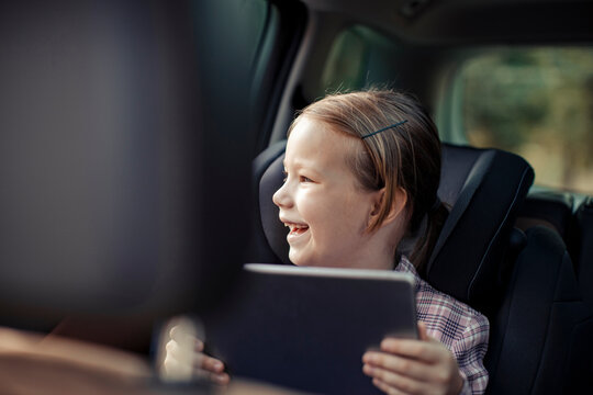 Smiling little girl in the car backseat with a tablet
