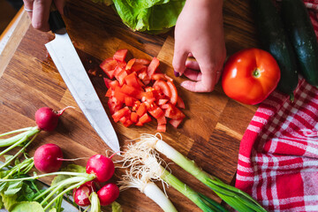 A close up of girl's or woman's hands cutting and peeling vegetables with knife making salad