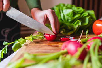 A close up of girl's or woman's hands cutting and peeling vegetables with knife making salad