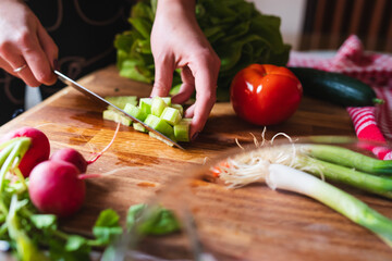 A close up of girl's or woman's hands cutting and peeling vegetables with knife making salad