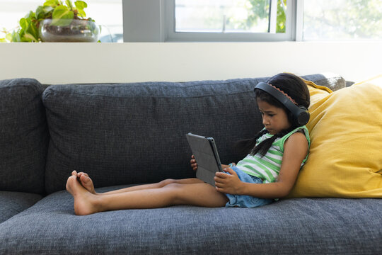 Biracial girl enjoys a tablet on a cozy sofa at home with copy space