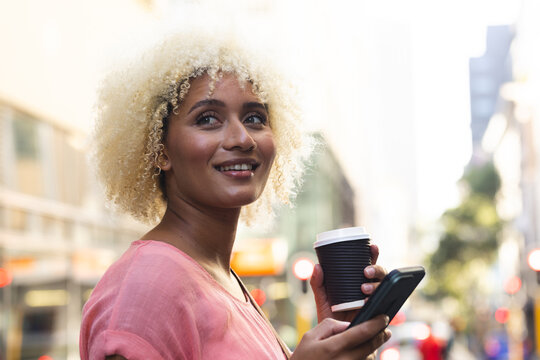 Young biracial woman enjoys a coffee outdoors in the city