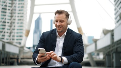 Smart business man wear headphone while sitting at stair in urban city and listen to relaxing...