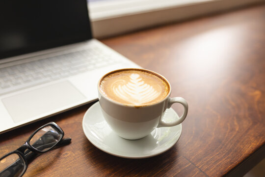 A cup of coffee sits near a laptop on a wooden table with copy space