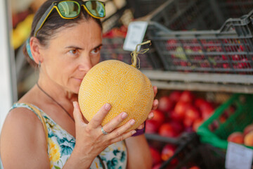 Mature woman choosing ripe melon in street shop in resort town. Summer healthy shopping in farm...