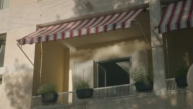 Terrace in the mediterranean village. Vacation balcony in the summer. White wodden shutters and flowers. Sun is creating shadows across the fasade. 