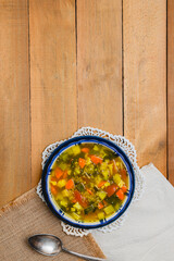 top view of one bowl of quinoa vegetable soup with spoon over wood board table with negative space