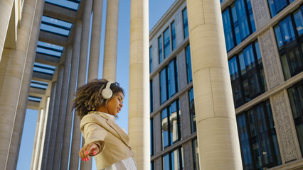 With headphones on and a radiant smile, a young professional woman dances freely in an urban space,...