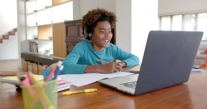 African american boy wearing headphones, using laptop for online class, slow motion