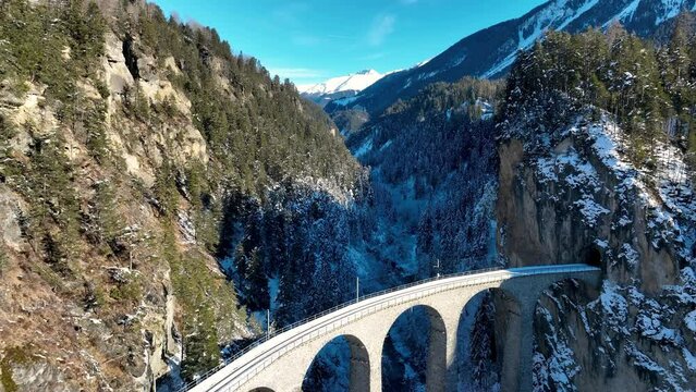 Aerial view of Landwasser Viaduct and Bernina express in Swiss Alps snow winter scenery. Drone shot red train passing through mountain in Filisur, Switzerland.