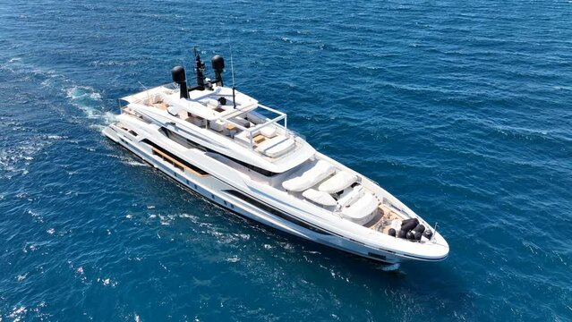 Aerial drone tracking photo of beautiful modern super yacht with wooden deck and helipad cruising in high speed deep blue open ocean sea