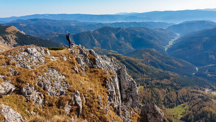 Fototapeta na wymiar Hiker man on edge of steep cliff on top of mountain peak Hohe Veitsch, Mürzsteg Alps, Styria, Austria. Idyllic hiking trail in alpine terrain. Wanderlust remote Austrian Alps in autumn. Rock formation