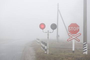 A railway crossing with a working semaphore and a stop sign. In the fog