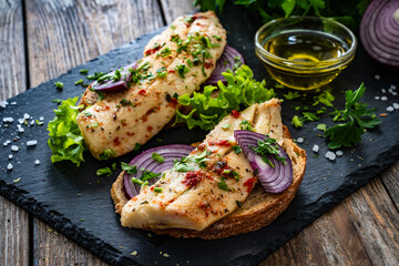 Tasty sandwiches - toasted bread with pickled herrings on and red onion on wooden table

