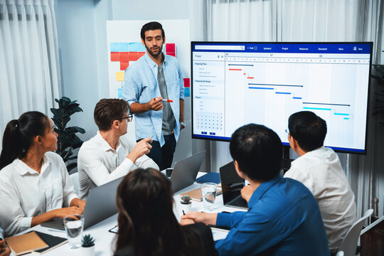 Project manager communicate and collaborate with team using project management software display on monitor, tracking progress of project task and making schedule plan at meeting table. Prudent