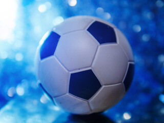 Fototapeta premium Classic soccer or football ball in focus. Busy background with glitter bokeh. Blue tone . Sport theme image.