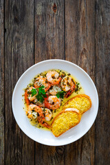 Fried shrimps with garlic and parsley in olive oil and toasted bread with parmesan cheese on wooden table