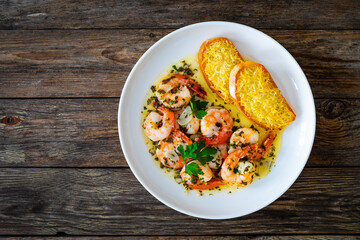 Fried shrimps with garlic and parsley in olive oil and toasted bread with parmesan cheese on wooden table