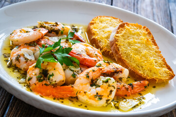 Fried shrimps with garlic and parsley in olive oil and toasted bread with parmesan cheese on wooden table