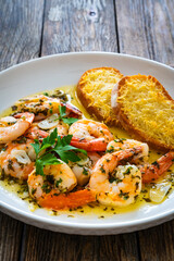 Fried shrimps with garlic and parsley in olive oil and toasted bread with parmesan cheese on wooden table