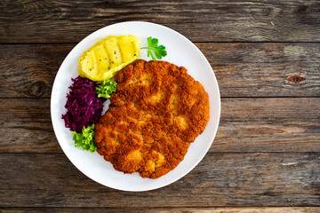 Crispy breaded fried pork chop with potato puree and cooked red cabbage on wooden table