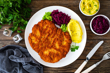 Crispy breaded fried pork chop with potato puree and cooked red cabbage on wooden table