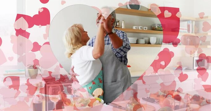 Animation of hearts over senior caucasian couple dancing in kitchen