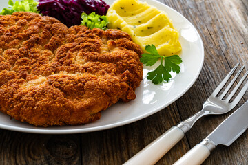 Crispy breaded fried pork chop with potato puree and cooked red cabbage on wooden table