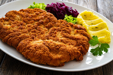 Crispy breaded fried pork chop with potato puree and cooked red cabbage on wooden table