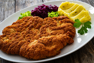 Crispy breaded fried pork chop with potato puree and cooked red cabbage on wooden table