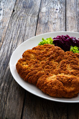 Crispy breaded fried pork chop with potato puree and cooked red cabbage on wooden table
