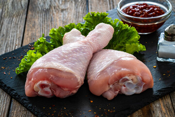 Raw chicken drumsticks on cutting board with seasonings on wooden table
