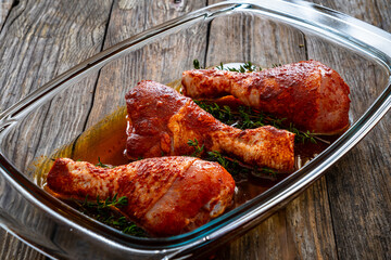 Raw seasoned chicken thighs in glass baking dish on wooden table
