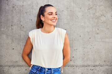 Portrait of smiling adult woman leaning against concrete wall looking away
