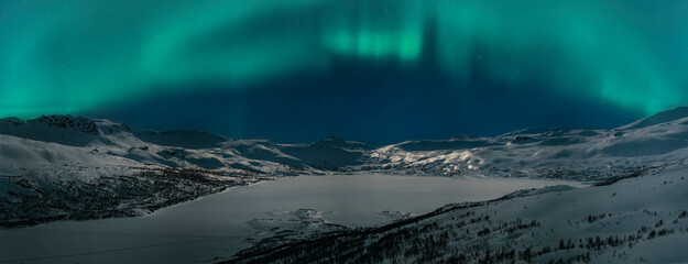 Wide scenic night panorama of winter mountains highlighted by Aurora Borealis green lights. Norway...