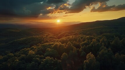 A bird's-eye view reveals a breathtaking sunset casting its warm, dramatic colors over forested hills, creating a scene of serene beauty and natural splendor. - obrazy, fototapety, plakaty