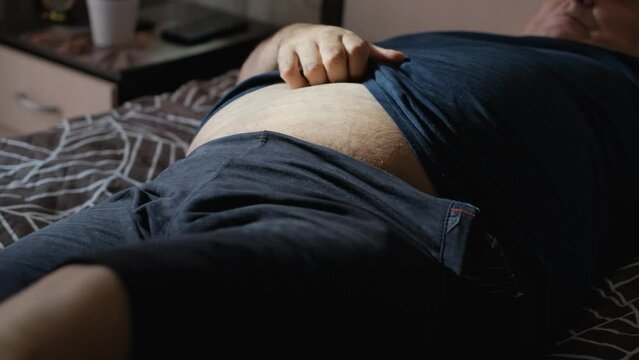 Fat lazy man scratches his huge belly with his hand