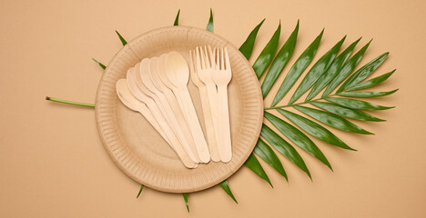Paper plates, wooden spoons and forks on a beige background