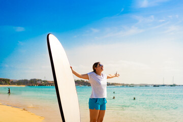Beautiful woman holding surfboard standing on sunny beach Santa Maria, Sal island , Cape Verde
