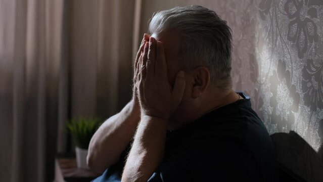 Elderly gray-haired man depressed sitting on bed at home
