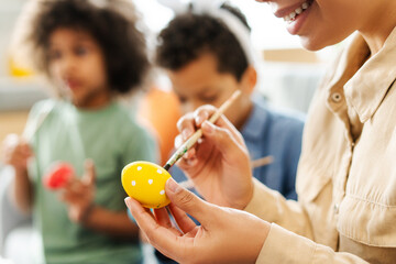 Closeup hands smiling mother and cute kids painting and decorating easter eggs at home, selective...